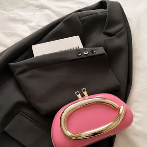 Magenta clutch with golden oval handle and chain strap on dark grey blazer outfit