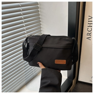 Détail du sac bandoulière en nylon noir avec étiquette logo en cuir marron mode