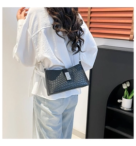 Detalle de bolso bandolera de tejido negro con cierre de metal plateado y correa de cadena
