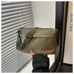 Détail du sac bandoulière en nylon vert armée montrant les fermetures éclair et l'étiquette