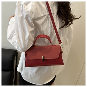 Détail du sac bandoulière rouge avec boucle dorée porté par un mannequin en style décontracté