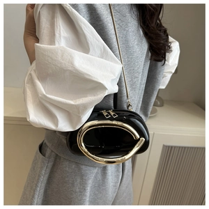 Detail of black patent leather semi-circular bag with large gold metal oval handle