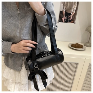 Detail of a black cylinder bag with oversized bow and metal buckle on the strap