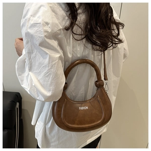 Détail du sac hobo marron foncé porté en bandoulière sur une chemise blanche