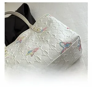 Gros plan sur un cabas blanc matelassé avec broderie papillon colorée et rivets métalliques