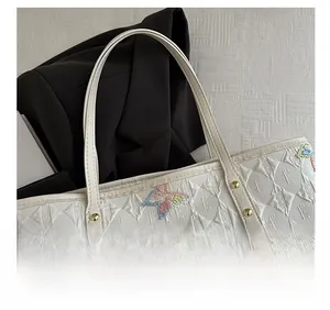 Détail du sac cabas blanc avec rivets dorés et motifs de papillons brodés élégants
