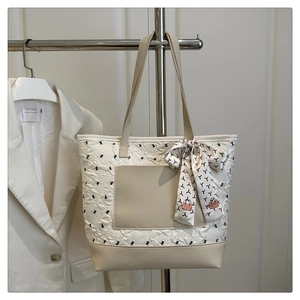Close-up of beige tote bag with floral quilted texture and decorative silk scarf handle