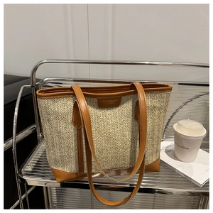 Détail du cabas en paille tissée avec poignées en cuir marron et écusson en cuir