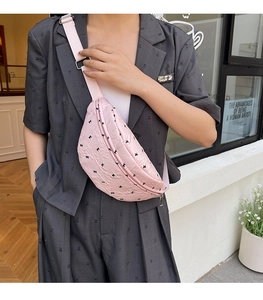 Detailed view of pink pleated chest bag with black bow patterns and adjustable strap