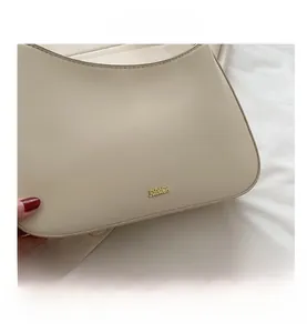Close-up of beige leather shoulder bag featuring a gold metal logo on smooth finish