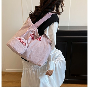 Pink canvas tote bag with red Beach text and matching drawstring pouch on shoulder