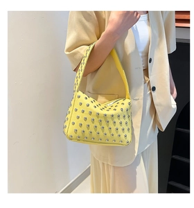 Dettaglio borsa sottobraccio in pelle giallo acceso con borchie argento e trama litchi