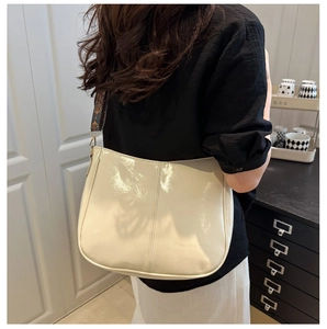 Detail of cream patent leather hobo bag with vintage textured wide shoulder strap