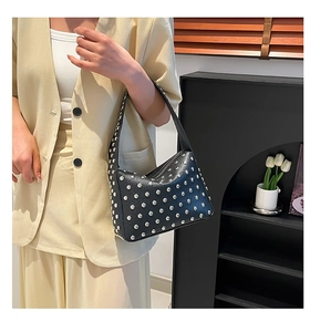 Detail of black glossy leather shoulder bag with silver rivet studs on female model