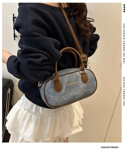 Detail of blue denim Boston bag with brown leather handles and adjustable shoulder strap