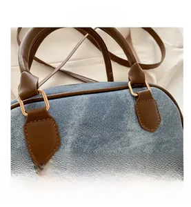 Detail of denim bowling bag with brown leather handles and golden D-ring hardware