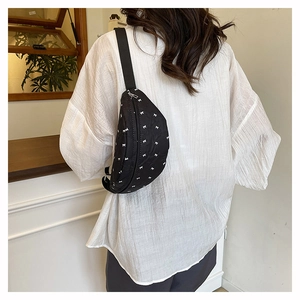 Close-up of quilted black crossbody bag with white bow pattern on a female model