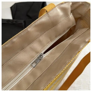 Detail shot of the large straw tote bag featuring a yellow canvas handle and silver zipper