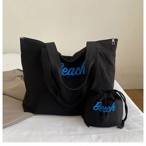 Detail view of black canvas tote bag set with blue Beach lettering and drawstring pouch