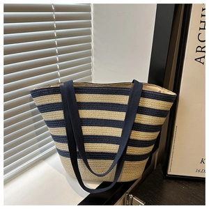 Detail of hand-woven straw tote bag with navy blue stripes and sturdy bamboo handle