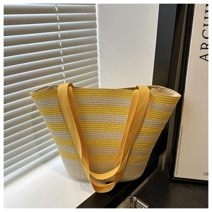 Detail of woven straw tote bag with yellow stripes and long fabric handles near a window