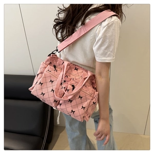 Pink corduroy shoulder bag with black diamond pattern and bow details worn by model