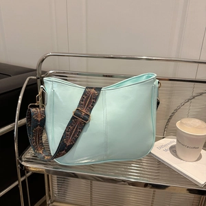 Stylish mint green PU leather crossbody bag with patterned wide strap on a metal stand