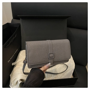 Détail d'un sac à main gris avec texture diagonale, sangle à boucle et fine bandoulière