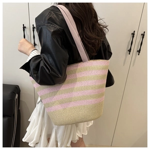 Pink and beige striped woven straw tote bag shown on shoulder in a casual setting