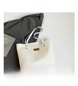 Détail de la texture tissée et de l'étiquette en cuir brun sur le grand sac cabas blanc