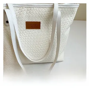 Détail du sac cabas blanc tissé avec des anses en similicuir et écusson logo de marque