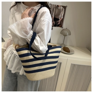 Sac cabas en paille rayé bleu marine et beige porté par un mannequin pour les vacances
