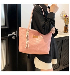 Détail du sac cabas rose tissé avec étiquette en cuir et pompon décoratif sur l'anse