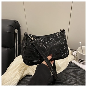 Detail of black snake pattern faux leather shoulder bag held by a person in a stylish setting