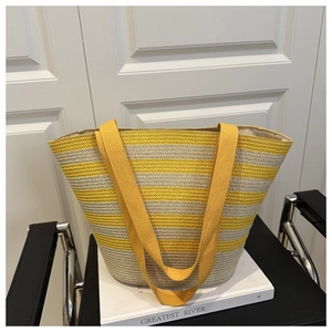 Detail of yellow and gray striped woven straw tote bag resting on a white book