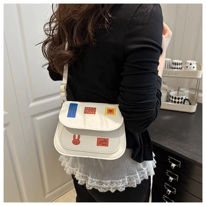 Vue détaillée du sac selle blanc avec des écussons de dessins animés et des cœurs