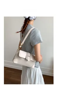 Model wearing a cream woven baguette shoulder bag with gold hardware from a back view