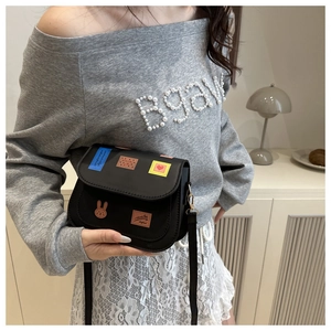 Detail of black saddle bag featuring colorful embroidery patches shown on model
