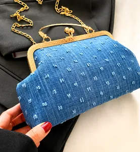 Détail du sac coquillage en denim bleu avec cadre en métal doré gravé et texture