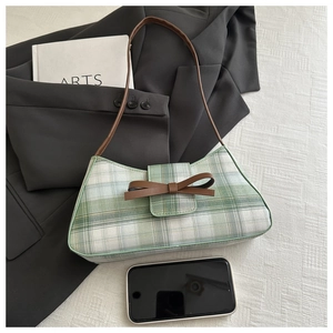 Detailed close-up of green checkered fabric and brown leather bow on an underarm bag