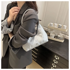 Silver snakeskin hobo bag shown on shoulder of model wearing a grey suit jacket