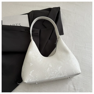 Macro detail of white snakeskin texture on hobo bag with metal feet on white tabletop