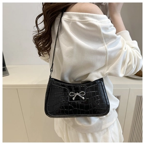 Detail of black faux crocodile leather underarm bag with silver bow accent on shoulder