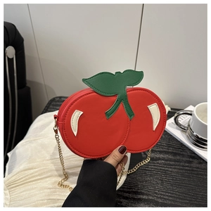 Detalle de un bolso bandolera creativo con forma de cereza roja y cadena de metal dorado