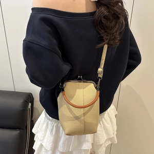 Détail du sac seau en toile avec poignée en cuir et fermoir kiss-lock porté par le mannequin