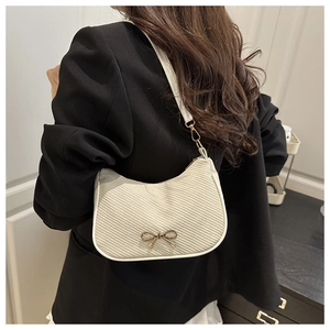 Detail of cream shoulder bag with golden bow and twill fabric texture on model
