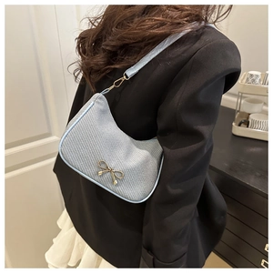 Close-up of light blue shoulder bag with golden bow hardware and textured finish