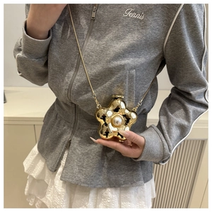 Detailopname van een gouden bloemvormige minitas met parel en fijne metalen ketting