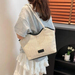Detail of beige straw tote bag with black trim and chunky rope straps on shoulder