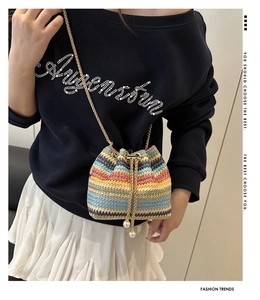 Detail view of woven bucket bag with colorful stripes, gold chain, and pearl charms